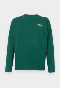 Ciemnozielona, długorękawowa koszulka typu crew neck z małym różowym i białym napisem graficznym na górnej lewej stronie klatki piersiowej.