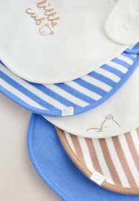Quatre bavoirs pour bébé empilés, comprenant un bavoir blanc avec le texte "little cub" et un ours, un bavoir à rayures bleues et blanches, un bavoir à rayures beiges et blanches avec un ours, et un bavoir bleu uni.