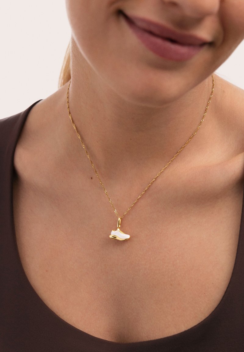 Collar de cadena de oro con un diseño retorcido que presenta un pequeño colgante de zapatilla blanca. Textura suave, detalle delicado en la zapatilla.