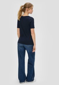 Marineblauw T-shirt met korte mouwen, aansluitende pasvorm, gecombineerd met wijdvallende blauwe jeans. Glad katoen met een eenvoudige constructie zonder patronen.