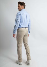 Lichtblauw geruit shirt met lange mouwen en knopenmanchetten, gecombineerd met crèmekleurige chino's en witte sneakers. Model vanachter gezien.