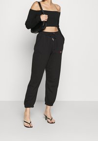 Black ribbed off-the-shoulder crop top paired with black drawstring sweatpants featuring side pockets and a colorful embroidered logo.