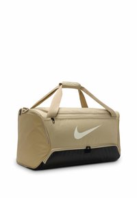Beige sporttas met een gestructureerd oppervlak, zwarte onderkant en een opvallend wit Nike-logo. Heeft dubbele handvatten en ritscompartimenten.