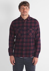 Chemise en flanelle à carreaux rouges et bleu marine, à manches longues, avec deux poches poitrine, fermeture à boutons et texture douce.