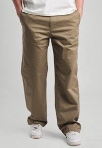 Lightweight, khaki pants with a loose fit, featuring side pockets and a smooth texture. Paired with white sneakers.