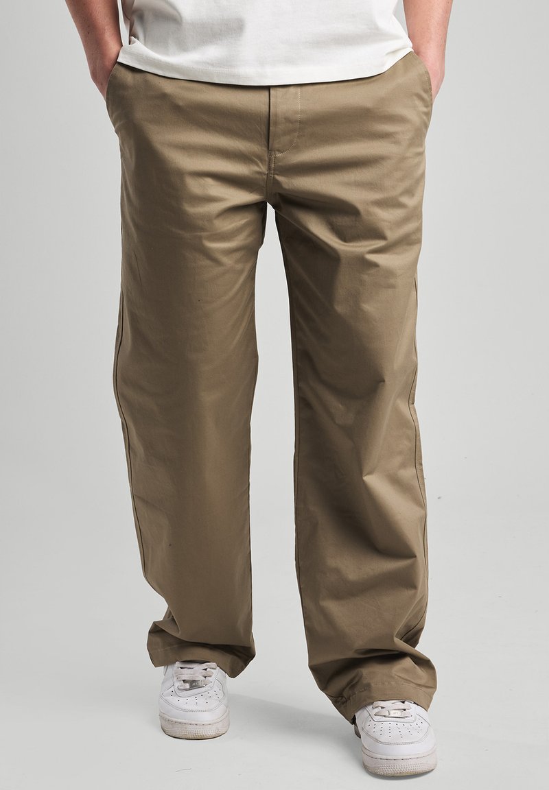 Lightweight, khaki pants with a loose fit, featuring side pockets and a smooth texture. Paired with white sneakers.