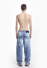 Široke plave traperice s blagim izbledjelim dijelovima, dvije stražnje džepove i jedinstvenim šavovima. Imaju crni akcent blizu struka.