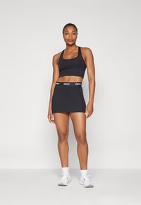 Top nero sportivo e gonna aderente abbinata con vita DKNY, indossati con sneakers bianche. Texture liscia, design minimalista.
