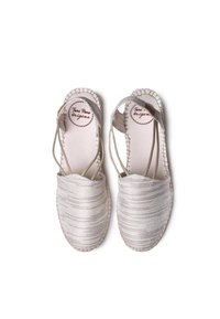Espadrilles de color beige claro con correas elásticas, un upper texturizado y detalles cosidos alrededor de la suela, que ofrecen un diseño tejido y natural.