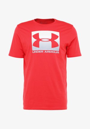 Czerwona koszulka z krótkim rękawem wykonana z bawełny, z dużym białym logo z napisem "UNDER ARMOUR" umieszczonym centralnie poniżej. Gładka faktura, okrągły dekolt.