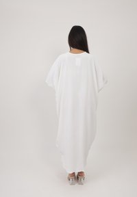 Robe maxi blanche avec une silhouette fluide et ample, des manches courtes et un tissu doux et léger. Présente un col rond et une longueur mi-mollet.