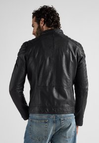 Zwarte leren motorjack met een strakke uitstraling, zichtbare stiknaden en geribbelde accenten op de schouders. Draagt met vervaagde blauwe jeans.