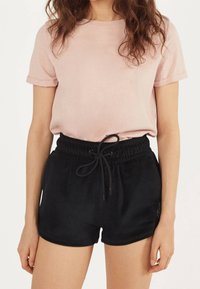 Ljusrosa t-shirt i bomull med uppvikta ärmar, tillsammans med svarta, mjuka tygshorts med dragsnodd som har en subtil detalj.