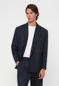 Navy pinstriped suit with a structured blazer featuring a single button and notch lapels, paired with a plain white T-shirt.