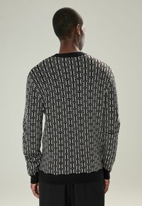 Pulover negru și gri cu model geometric, textură tricotată, guler rotund și manșete și tiv cu nervuri. Vederea din spate arată un design distinct.