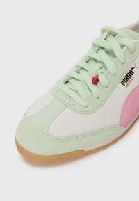 Puma tenisice s gornjim dijelom od mente zelene kože, ružičastim detaljima, bijelim kožnim panelima, ukrašene zelenim vezicama i privjeskom u obliku jagode.