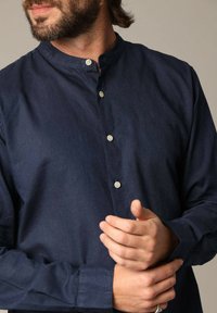 Marineblauwe langekleding shirt van lichtgewicht stof, met een mandarinnekraag en een frontale knoopsluiting met lichtgekleurde knopen.