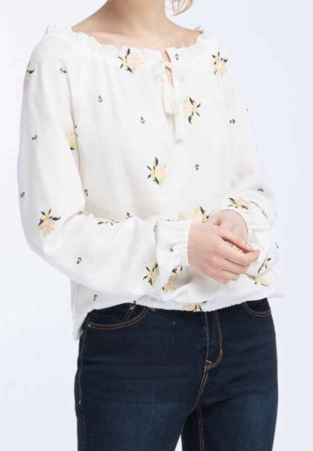Blusa bianca a maniche lunghe con motivi floreali e piccoli ancore. Presenta una scollatura a chiave e dettagli con polsini elasticizzati.