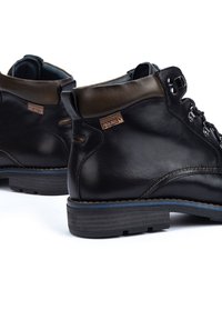 Bottines en cuir noir avec des accents marron, des lacets robustes et des semelles texturées. Présente une petite étiquette de marque sur le côté.