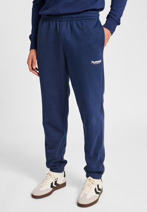 Marineblaue Jogginghose mit elastischem Bund, seitlichen Taschen und einem kleinen weißen Logo. Der Stoff wirkt weich und texturiert.