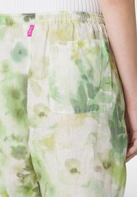 Lichte linnen broek met een pastelgroen bloemenpatroon. Voorzien van een elastische tailleband en een patchzak aan de rechterkant.
