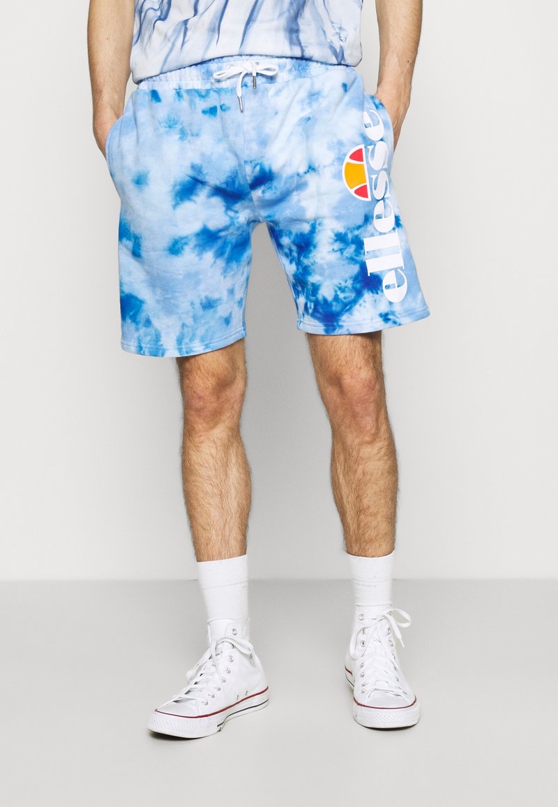 Shorts tie-dye bleus en mélange de coton, dotés d'une taille à cordon de serrage et d'un logo blanc. Associés à des baskets blanches et des chaussettes blanches.