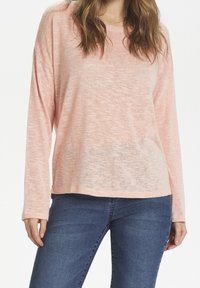Jasnoróżowa bluzka z długim rękawem o luźnym kroju i textured tkaninie, w połączeniu z niebieskimi dżinsami. Prosty, casualowy design bez zdobień.