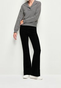 Jean noir évasé associé à un pull à rayures à manches longues avec un col large. La tenue est complétée par des baskets blanches.