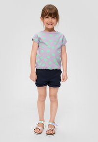 Paars T-shirt met korte mouwen met groene palmboomprint, gecombineerd met donker marineblauwe shorts en bruine sandalen met reflecterende accenten.