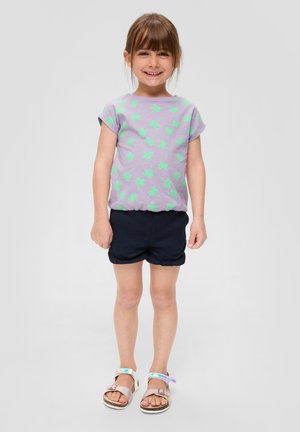 Lila kurzärmliges T-Shirt mit grünem Palmen-Print, kombiniert mit dunkelblauen Shorts und braunen Sandalen mit reflektierenden Akzenten.