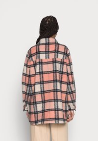 Flanelová košile s podšívkou v růžovém, krémovém a šedém kostkovaném vzoru. Obsahuje límec, dlouhé rukávy a volný střih se bočními rozparky.