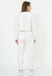 Weißer, kurzer Sweatshirt, kombiniert mit weißen Jogginghosen, die elastische Bündchen und einen elastischen Bund haben, mit glatter Textur und minimalistischem Design.