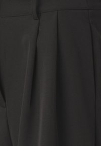 Pantaloni neri realizzati in tessuto liscio e texturizzato con pieghe frontali e una vita sartoriale. Design semplice e sobrio senza decorazioni.