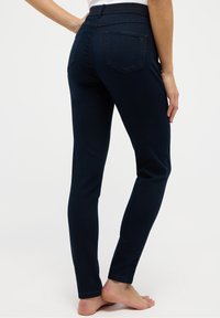 Tmavě modré džíny s úzkým střihem, vysokým pasem a dvěma zadními kapsami. Materiál působí hladce a pružně, s čistým zakončením okrajů.