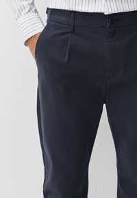 Pantalon bleu marine en tissu léger, doté de poches latérales, d'une taille plate et d'une coupe ajustée. Texture lisse avec une finition nette.