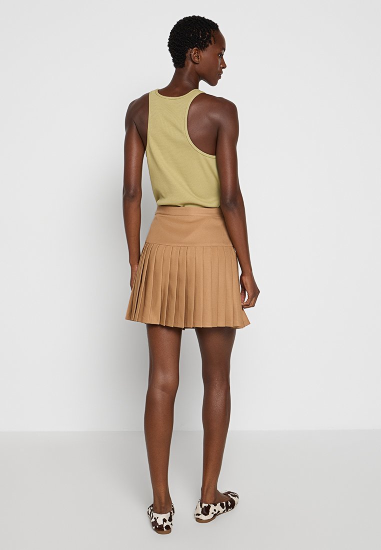 Gonna plissettata beige con vita alta, abbinata a un top senza maniche verde chiaro. Modella che indossa scarpe slip-on con stampa animale.