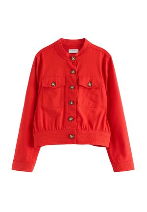 Punainen lyhyt takki pitkillä hihoilla, kahdella rintataskulla, pyöreällä kauluksella ja seitsemällä ruskealla napilla edessä.