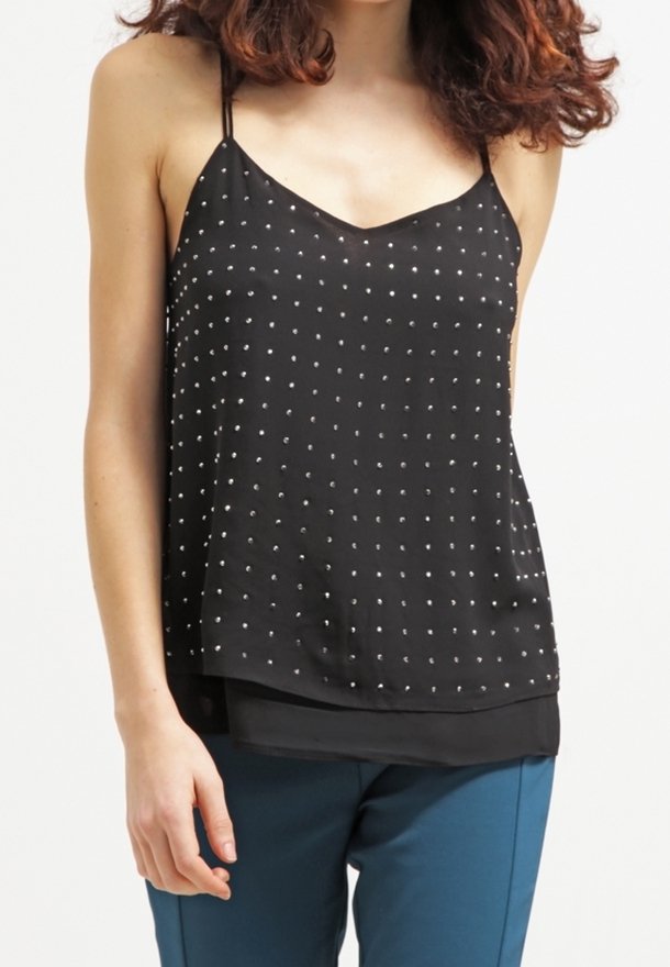 Femme portant un top noir sans manches avec de fines bretelles et de petits pois blancs, associé à un pantalon bleu.