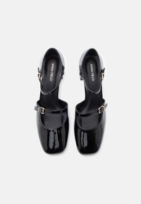 Black patent leather Mary Jane shoes with square toes, two buckle straps, and low block heels, branded with Anna Field.