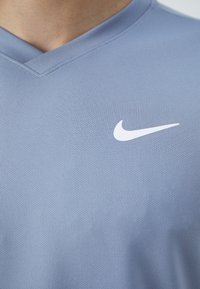 Vaaleansininen Nike-urheilupaita, joka on valmistettu teksturoidusta kankaasta, jossa on V-pääntie ja valkoinen Nike-swoosh-logo rinnassa.