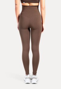 Leggings marron taille haute en matière extensible, dotés d'un design sans coutures et de surpiqûres contrastées, associés à des baskets blanches.