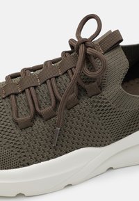 Dark green textured knit sneaker featuring a lace-up design with brown elastic straps and a white, chunky sole.