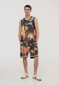 Outfit in stile basket con canotta senza maniche in rete e pantaloni abbinati. Entrambi i pezzi presentano una vivace stampa di palme in arancione e nero.