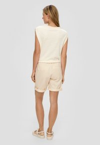 Beżowo-kremowy top bez rękawów w paski, zestawiony z jasnobeżowymi szortami z podwiniętymi nogawkami i miękką teksturą materiału.