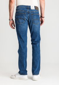 Niebieskie dżinsy z denimu o prostym kroju, z naszywką na tylnej części pasa, dwoma tylnymi kieszeniami z przeszyciami w zygzak oraz wyraźnie postarzaną teksturą.