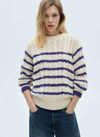 Maglione lavorato a maglia crema con strisce viola, caratterizzato da un motivo a treccia, polsini e orlo a coste. Abbinato a jeans scuri.