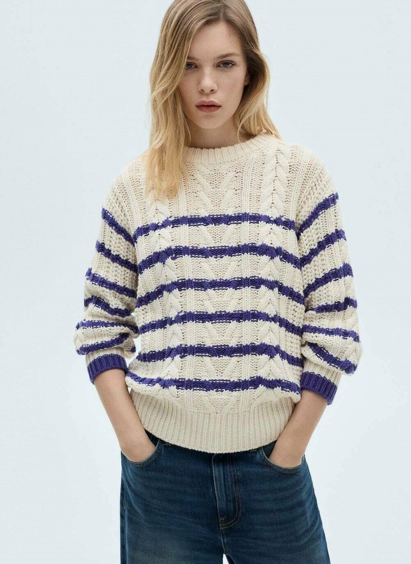Maglione lavorato a maglia crema con strisce viola, caratterizzato da un motivo a treccia, polsini e orlo a coste. Abbinato a jeans scuri.