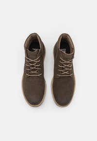Botas de ante marrón hasta el tobillo con punteras redondas y cordones beige, con un acabado texturizado y suelas de goma de color claro.