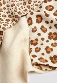 Leopardprintstof in bruintinten op een lichtbeige achtergrond, met een zachte textuur en een lichte doorzichtigheid, en variërende patronen.
