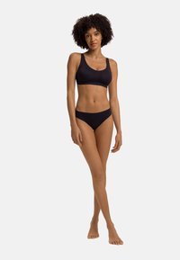 Schwarze Bikini mit einem nahtlosen, glatten Stoff. Der Bralette hat ein breites Band und dicke Träger, während der Unterteil einen klassischen Schnitt hat.